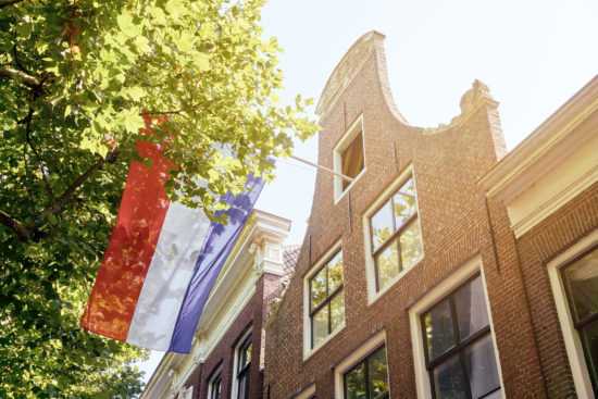 Facade of house and green tree in the Netherlands with dutch flag on a sunny day